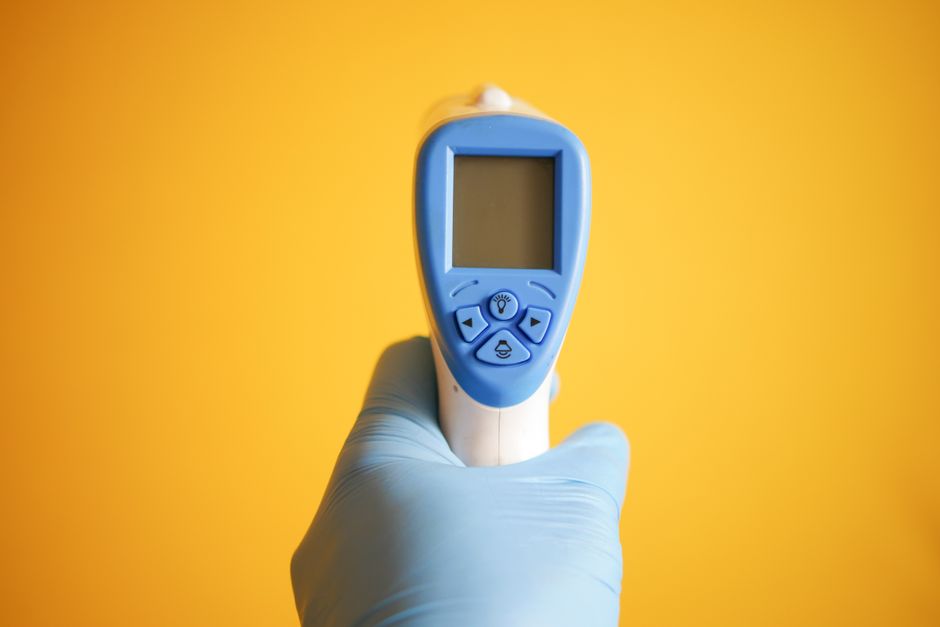 Close-up of a gloved hand holding a digital thermometer against a bright yellow background.